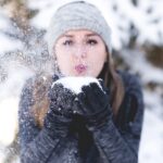 teple oblečená žena v zimě fouká do sněhové koule