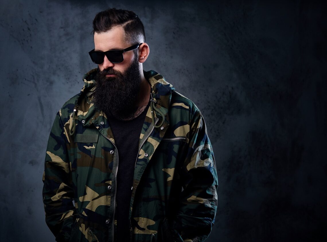 A man dressed in a camouflage jacket over grey background.